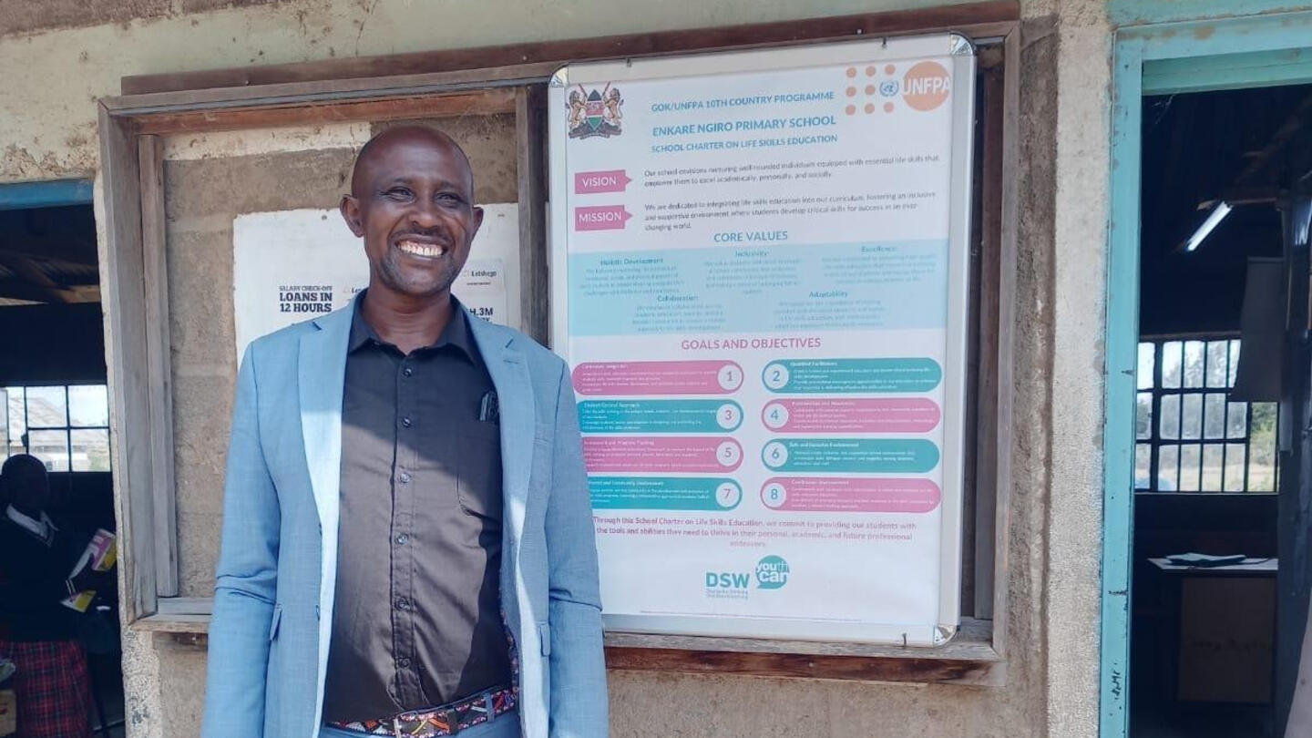 David Kirempe, headteacher of Enkare Ngiro School in Narok stands next to the school charter for life skills.